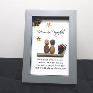 May include: A framed pebble art piece with a gray frame and a white background. The art features two figures made of pebbles, a small evergreen sprig with red berries, and gold stars. The text reads "Mum & Daughter" and "No matter where we go, no matter what we do, you will always have me and I will always have you."