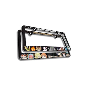 May include: Two black license plate frames with a decorative border featuring cartoon characters. The top frame has Japanese text. The bottom frame has a row of cartoon faces. The frames are rectangular with rounded corners.