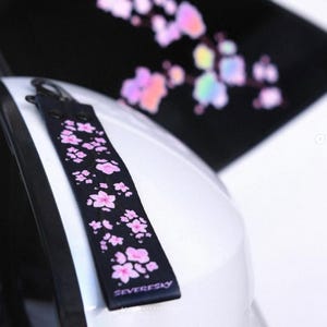 May include: Black keychain with a pink cherry blossom design and the word "SEVERESKY" printed on it.