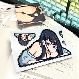 May include: A sticker featuring a cartoon illustration of a woman with long black hair and blue eyes. She is wearing a light blue shirt and is lying down. The sticker is on a white background.