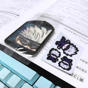 May include: A set of four stickers featuring a cartoon character with white hair, a black eye mask, and a dark blue outfit. The stickers are on a white background.