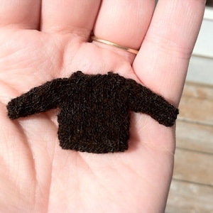 May include: A small brown knitted sweater, shown in the palm of a hand.