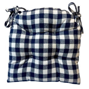 May include: A square cushion with a navy blue and white checkered pattern. The cushion has ties on each corner. The fabric is a soft material. The cushion is designed for a chair.