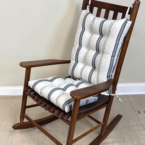 May include: A wooden rocking chair with a striped cushion. The chair is made of dark wood and has a slatted seat and back. The cushion is white with vertical navy blue stripes. The chair has armrests and is designed for comfort.