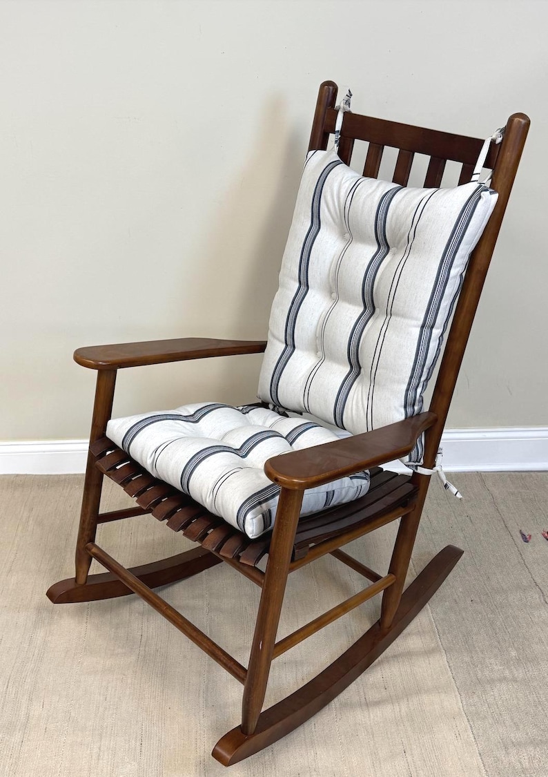 May include: A wooden rocking chair with a striped cushion. The chair is made of dark wood and has a slatted seat and back. The cushion is white with vertical navy blue stripes. The chair has armrests and is designed for comfort.