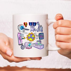 K&ouml;nnte beinhalten: Wei&szlig;e Keramiktasse mit einem bunten Cartoon-Design von medizinischen Ger&auml;ten, darunter ein R&ouml;ntgenapparat, ein CT-Scanner und ein Strahlungssymbol.