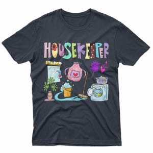 May include: A dark blue t-shirt with the word "HOUSEKEEPER" in rainbow colors. The shirt features a cartoon illustration of cleaning supplies, including a broom, a bucket, a spray bottle, a mirror, an apron, and a washing machine.