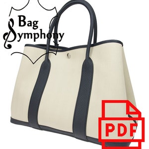 May include: A large, beige canvas tote bag with black leather trim and handles. The bag has a top zipper closure and a single, silver-toned hardware detail on the front.