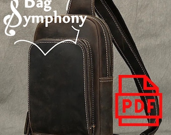 May include: A brown leather crossbody bag with a zipped pocket on the front and a large zipped compartment. The bag has a long adjustable strap and a metal buckle. The bag is made by Bag Symphony.