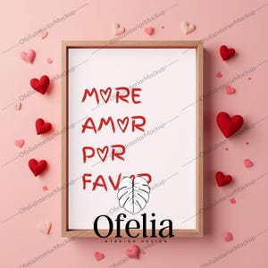 May include: A white framed picture with a pink background. The picture has the text "MORE AMOR POR FAVOR" written in red. Below the text is a black and white illustration of a leaf. The text "Ofelia INTERIOR DESIGN" is written in black below the leaf.