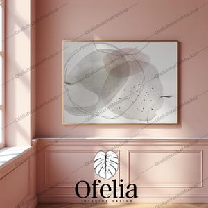 May include: A pink room with white trim and a framed abstract painting with gray and black watercolor shapes. The painting is hanging on the wall above a white wainscoting panel. The room has a large window with sunlight streaming in. The text "Ofelia Interior Design" is printed below a stylized leaf design.