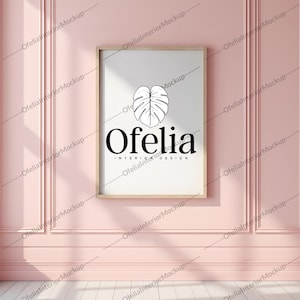 May include: A framed print with a minimalist design featuring a black leaf and the text "Ofelia Interior Design". The print is hanging on a pink wall with white trim.