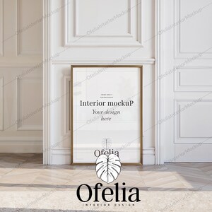Può includere: Un mockup di design d'interni incorniciato in oro con il testo "Interior mockup" e "Your design here" in una stanza bianca con modanature bianche e un tappeto bianco. Il testo "Ofelia" è sotto la cornice.