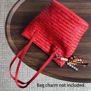Peut inclure: Un sac fourre-tout rouge vif tiss&eacute; avec des anses assorties. Le sac a une forme rectangulaire et une surface textur&eacute;e. Un charm d&eacute;coratif avec des perles est suspendu &agrave; un anneau m&eacute;tallique attach&eacute; au sac. Le texte "Bag charm not included" est en bas.
