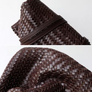 Peut inclure: Gros plan sur un sac en cuir tress&eacute; marron fonc&eacute;. Le sac est enroul&eacute; et s&eacute;curis&eacute; par une sangle en cuir assortie. Le motif de tissage est complexe et d&eacute;taill&eacute;, mettant en valeur le savoir-faire.