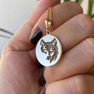 Op de afbeelding: Een gouden ketting met een ronde hanger met een wolfsilhouet. De hanger is gegraveerd met een wolfskop.
