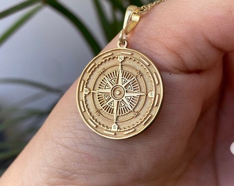 May include: Gold compass pendant necklace with a detailed design. The compass features the cardinal directions, north, south, east, and west.
