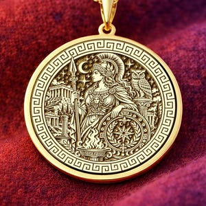 Puede incluir: Un colgante circular de tono dorado en una cadena fina con un diseño en relieve de una figura con casco que sostiene una lanza y un escudo, acompañada por un búho y columnas, todo enmarcado por un borde de greca clásica.