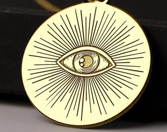 Puede incluir: Collar de oro con un colgante redondo que presenta un ojo con líneas radiantes. El ojo es negro con una pupila amarilla.