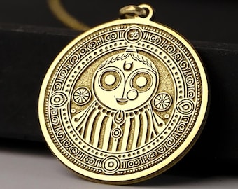 Puede incluir: Un collar con un colgante de oro de diseño circular que presenta una cara estilizada con detalles intrincados. El colgante está rodeado de círculos concéntricos de patrones geométricos.