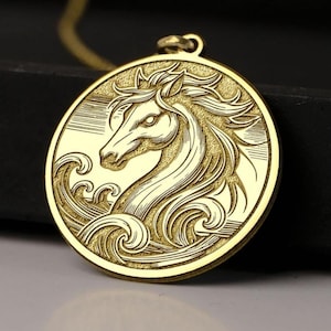 May include: A gold-colored pendant necklace featuring a detailed relief of a horse's head within a circular frame. The horse is depicted with flowing mane and is surrounded by stylized waves. The pendant hangs from a delicate gold chain.
