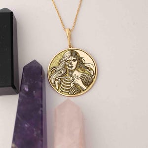 May include: A gold necklace with a round pendant featuring a detailed engraving of a woman's face and a skeleton, representing the duality of life and death.