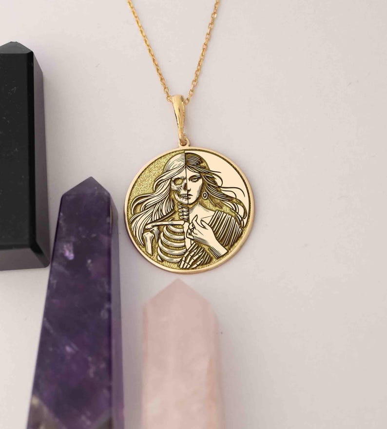 May include: A gold necklace with a round pendant featuring a detailed engraving of a woman's face and a skeleton, representing the duality of life and death.