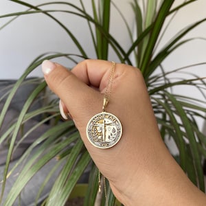 May include: Gold necklace with a round pendant featuring the words "Amor Faith" in a circle with a cross and floral design.