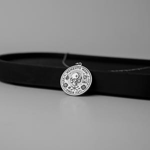 May include: A silver pendant necklace with a round charm featuring a skull, crossbones, hourglass, and the text "Memento Mori Amor Fati".