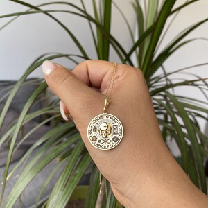 May include: Gold necklace with a round pendant featuring a skull and the text "Memento Mori Amor Fati".