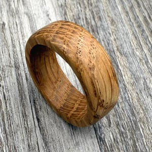 Könnte beinhalten: Ein Ring aus hellbraunem Holz mit einer ausgeprägten, natürlichen Maserung und sichtbaren dunkelbraunen Flecken und Streifen auf der gesamten Oberfläche, die die organische Textur und die Kreisform des Holzmaterials unterstreichen.