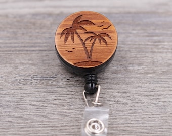 May include: A wooden retractable badge holder with a laser engraved design of two palm trees and birds. The holder is black and has a clear plastic strap.