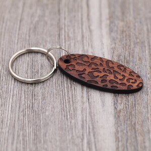 May include: A wooden keychain with a brown leopard print design. The keychain has a silver metal ring.