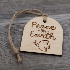 May include: A wooden ornament with a dove and the text "Peace on Earth" in a cursive font. The ornament is attached to a twine string.