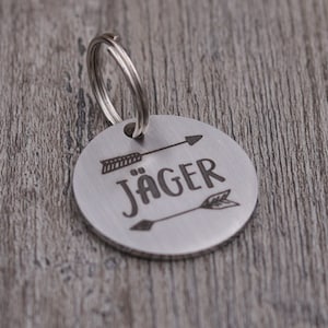 Könnte beinhalten: Silbernes Hundehalsband mit einem schwarzen Pfeil und dem Namen "Jäger" eingraviert.