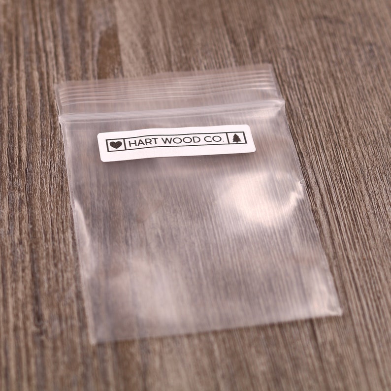 K&ouml;nnte beinhalten: Eine durchsichtige Plastikt&uuml;te mit einem wei&szlig;en Etikett, auf dem "HART WOOD CO." mit einem Herz und einem Kiefernbaum-Symbol steht.