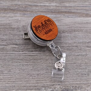 May include: A wooden badge reel with a clear plastic casing. The wooden disc features a design of hands signing the name "KERRI" in American Sign Language.