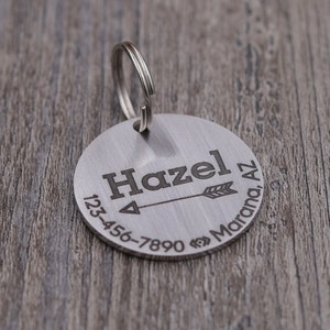 Könnte beinhalten: Silbernes Hundehalsband mit Pfeilmotiv, dem Namen "Hazel", einer Telefonnummer und dem Ort "Marana, AZ".