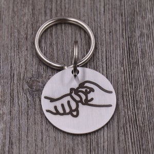 May include: Silver keyring with a round tag featuring a black outline of two hands holding each other.