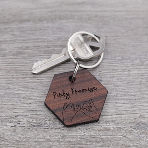 May include: A wooden hexagonal keychain with the text "Pinky Promise" and a drawing of two hands making a pinky promise.