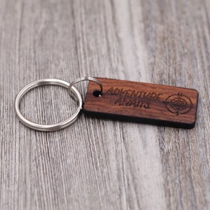 May include: Wooden keychain with a compass design and the text "Adventure Awaits".