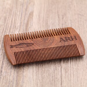 May include: A brown wooden comb with a fish design and the initials "ARH" engraved on the handle.
