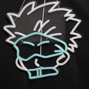 May include: White neon sign with a cartoon character wearing a blue mask. The character has spiky hair and a mischievous expression.
