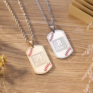 May include: Two gold and silver baseball-themed dog tag necklaces. The gold necklace has a tag with the number 34 and the name Nolan. The silver necklace has a tag with the letter R and the name Randy.