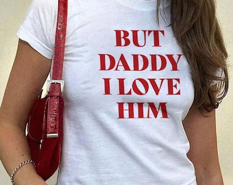 Puede incluir: Camiseta blanca recortada con el texto "BUT DADDY I LOVE HIM" impreso en rojo.