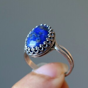 May include: A silver ring with a blue lapis lazuli stone set in a decorative silver bezel. The ring is oval shaped and has a delicate, ornate design.