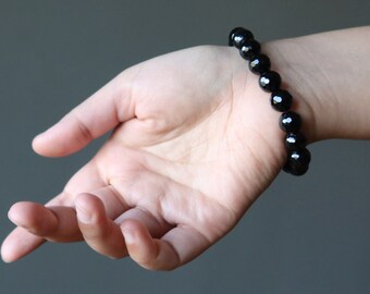 Puede incluir: Un brazalete negro de cuentas en la muñeca de una persona. El brazalete está hecho de cuentas redondas y facetadas.