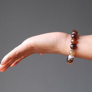 May include: A brown, white, and beige beaded bracelet on a person's wrist.
