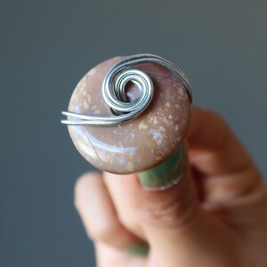 May include: A close-up of a ring with a brown and white agate stone wrapped in silver wire. The wire is twisted into a spiral design.