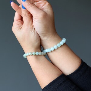 May include: Two bracelets made of light green gemstone beads on a person's wrists.